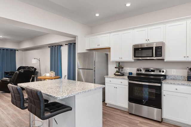 kitchen featuring light stone countertops, white cabinets, light wood-type flooring, and appliances with stainless steel finishes