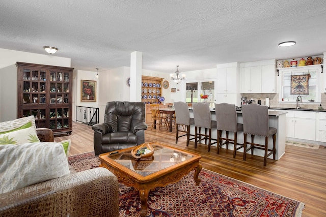  - living area featuring light wood-style flooring, a chandelier, and a textured ceiling