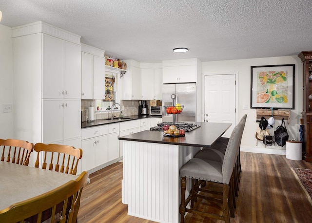  - kitchen featuring appliances with stainless steel finishes, a sink, dark countertops, wood finished floors, and a kitchen island