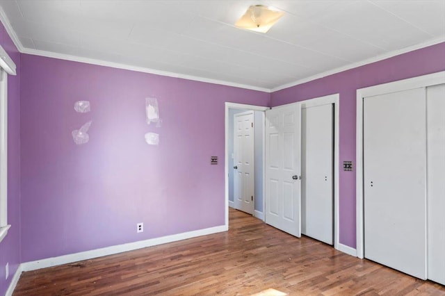 unfurnished bedroom with wood-type flooring, crown molding, and two closets