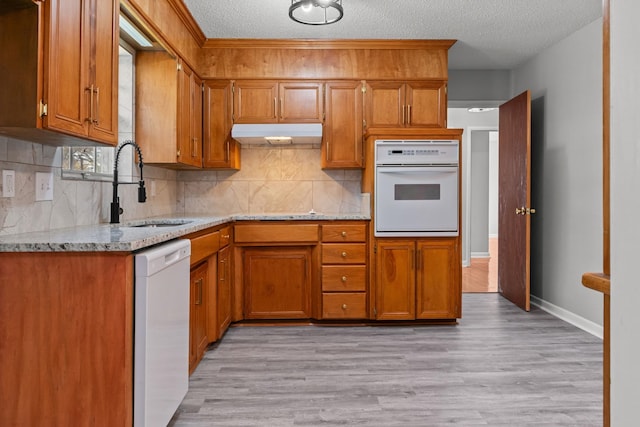  - kitchen with white appliances, a sink, brown cabinetry, a textured ceiling, and backsplash