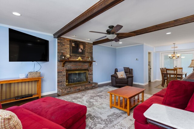 living room with ceiling fan with notable chandelier, ornamental molding, a fireplace, beam ceiling, and wood-type flooring