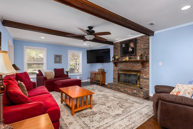 living room with ornamental molding, ceiling fan, hardwood / wood-style flooring, beamed ceiling, and a fireplace