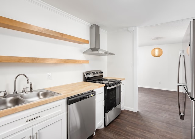 kitchen with dark wood-type flooring, wall chimney exhaust hood, sink, stainless steel appliances, and white cabinets