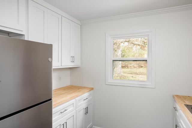 kitchen with white cabinetry, stainless steel fridge, butcher block countertops, and crown molding