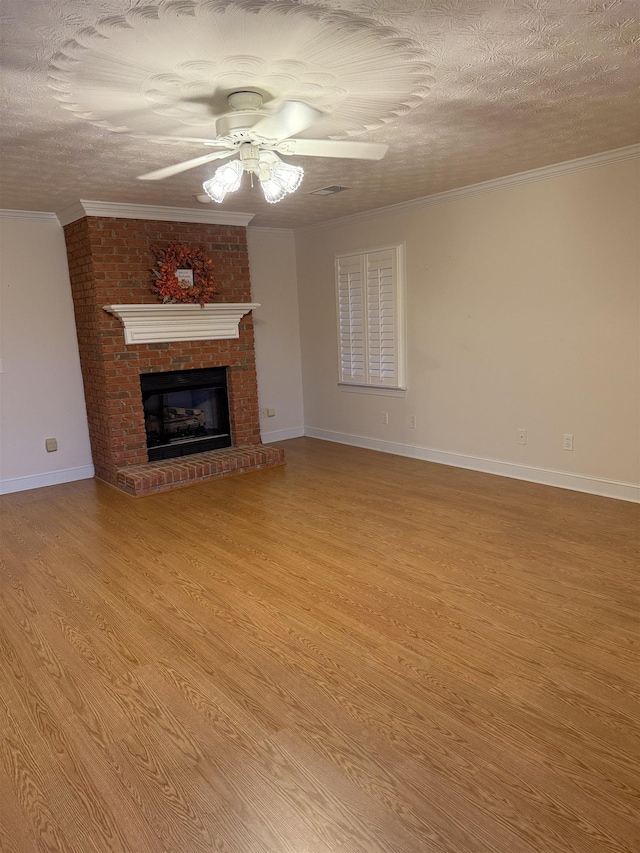 unfurnished living room with a brick fireplace, ceiling fan, light wood-type flooring, ornamental molding, and a textured ceiling