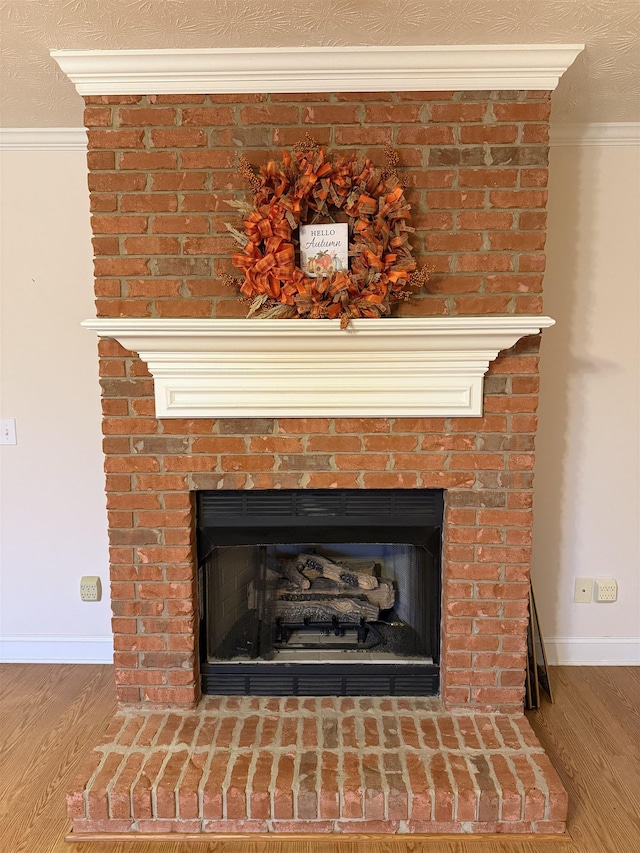 details featuring a textured ceiling, wood-type flooring, crown molding, and a brick fireplace