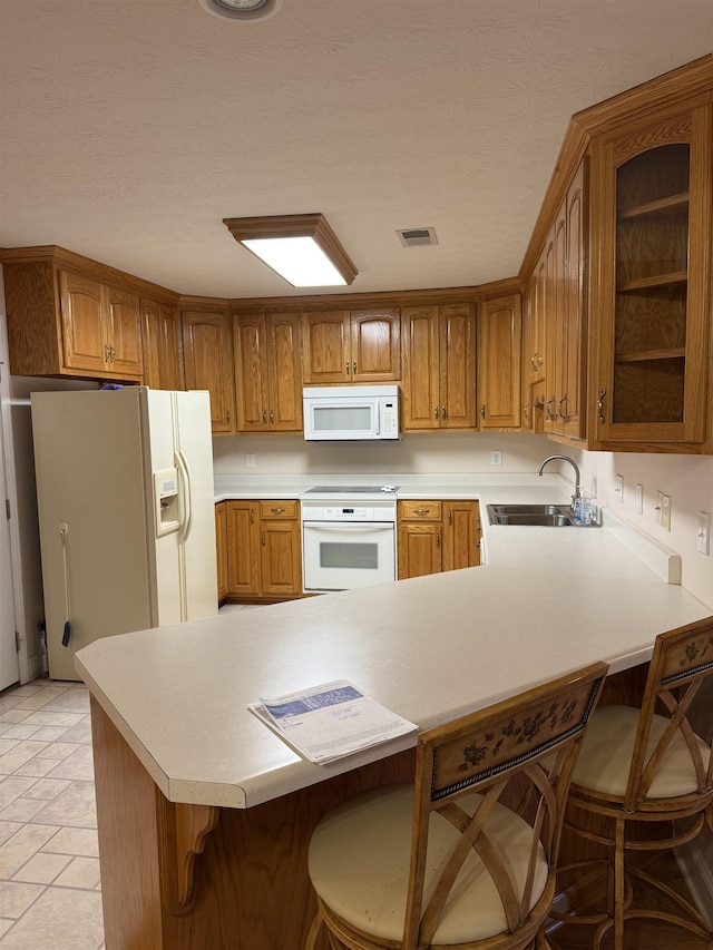 kitchen featuring a kitchen bar, kitchen peninsula, sink, and white appliances