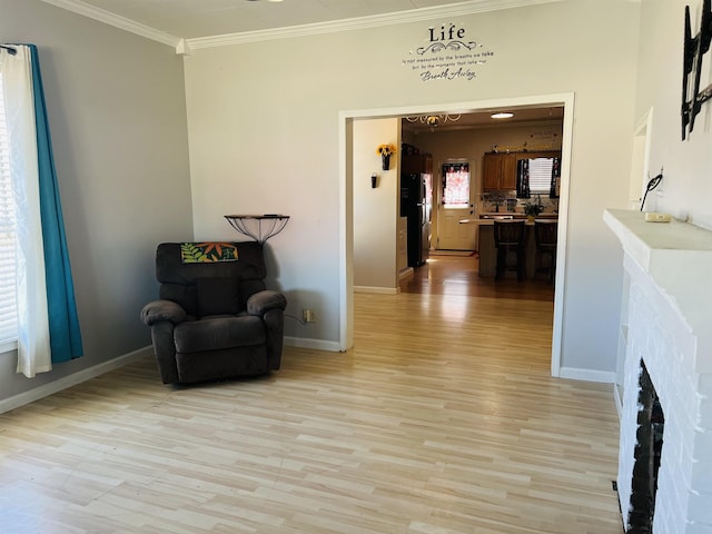 sitting room with a brick fireplace, light wood-type flooring, and crown molding