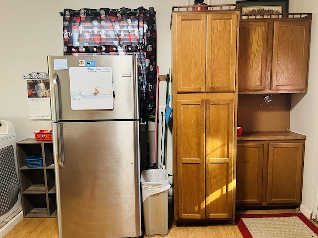 kitchen with stainless steel refrigerator, washer / clothes dryer, and light hardwood / wood-style flooring