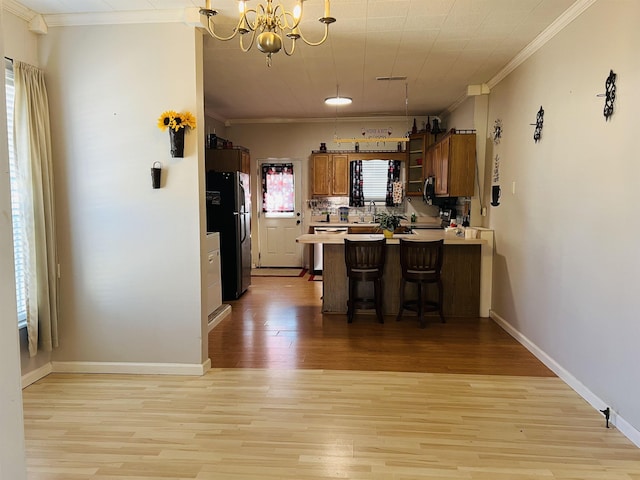 kitchen with kitchen peninsula, stainless steel dishwasher, black fridge, light hardwood / wood-style floors, and a kitchen bar