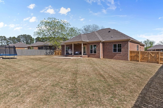 back of property with a fenced backyard, brick siding, a patio area, a lawn, and a trampoline