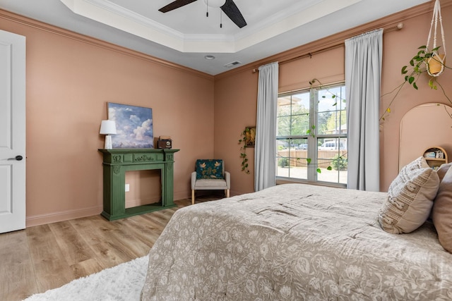 bedroom featuring visible vents, wood finished floors, a raised ceiling, baseboards, and ornamental molding