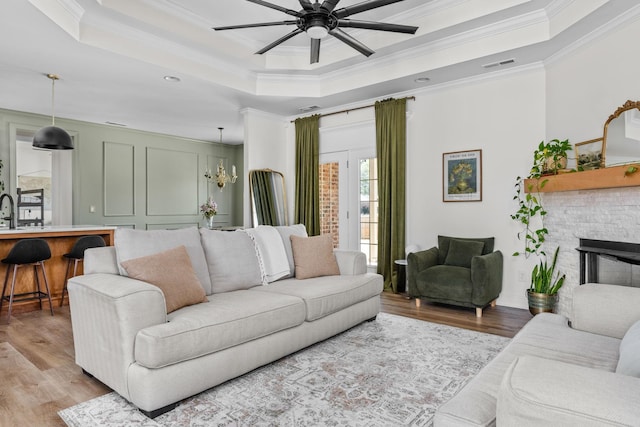 living area featuring visible vents, crown molding, light wood-style floors, ceiling fan, and a tray ceiling