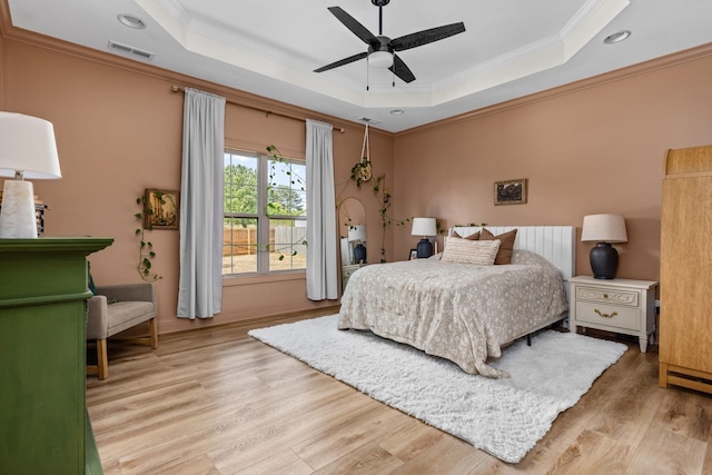bedroom with crown molding, wood finished floors, a tray ceiling, and visible vents