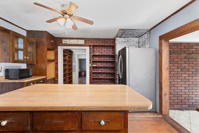 kitchen with brick wall, a textured ceiling, and stainless steel refrigerator