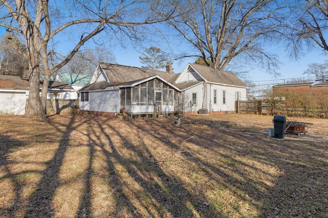 rear view of property featuring central air condition unit, a sunroom, and a lawn