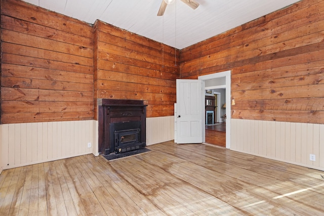 unfurnished living room with radiator, ceiling fan, hardwood / wood-style floors, wooden walls, and a wood stove