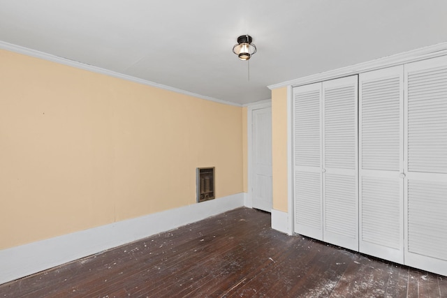 unfurnished bedroom featuring heating unit, dark wood-type flooring, ornamental molding, and a closet