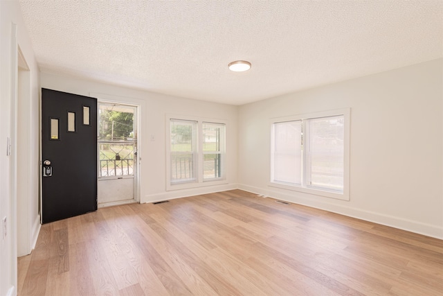 foyer entrance featuring light wood-style flooring, a textured ceiling, and baseboards