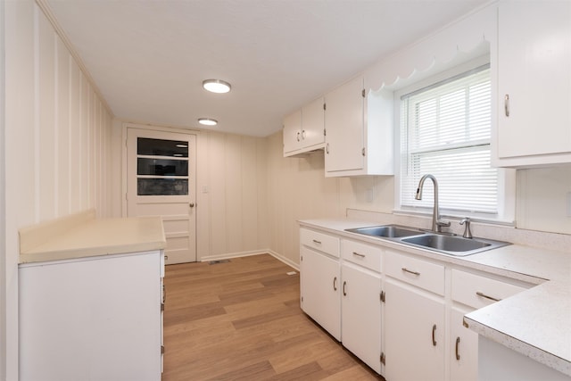 kitchen with a sink, light wood-type flooring, white cabinetry, and light countertops