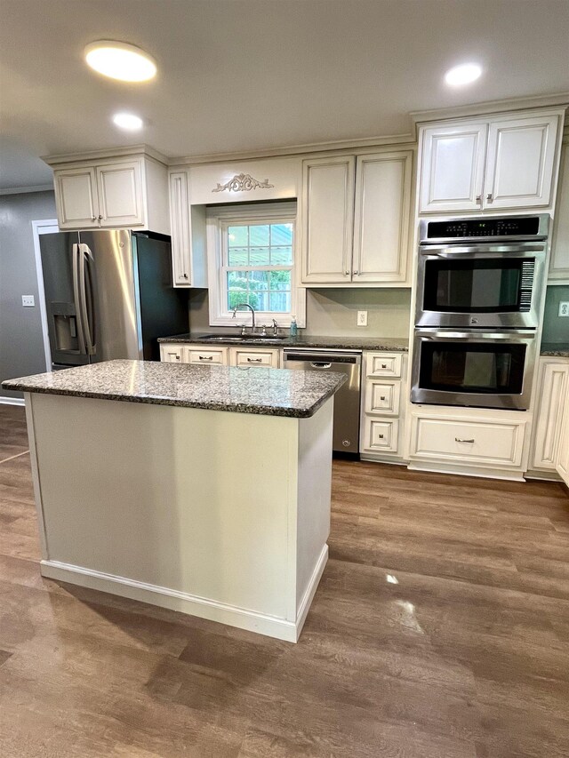 kitchen with dark stone counters, sink, dark hardwood / wood-style floors, a kitchen island, and stainless steel appliances