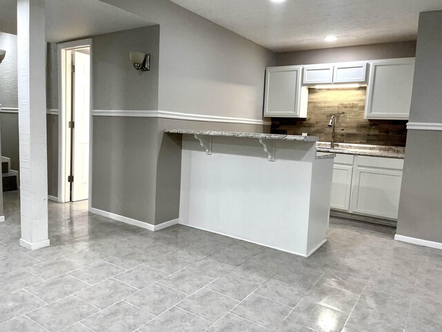 kitchen featuring tasteful backsplash, light stone counters, sink, white cabinetry, and a breakfast bar area