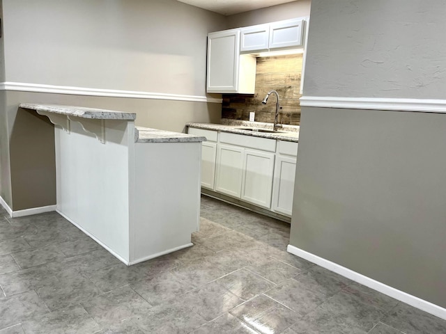 kitchen with sink, kitchen peninsula, a breakfast bar area, decorative backsplash, and white cabinets