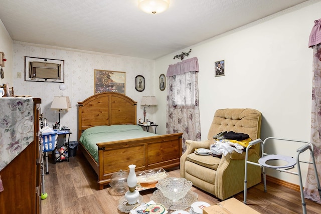 bedroom with wood finished floors, a wall unit AC, baseboards, and wallpapered walls