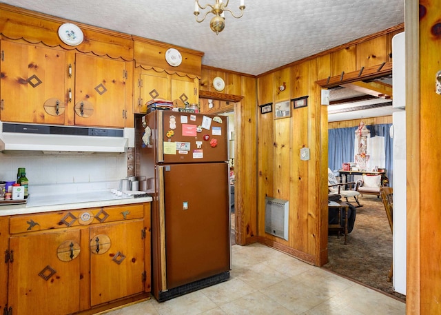kitchen with under cabinet range hood, freestanding refrigerator, brown cabinets, wood walls, and light countertops