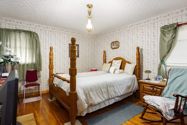 bedroom featuring wood finished floors, wallpapered walls, and a textured ceiling