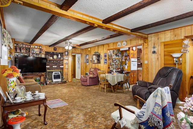 living area with wood walls, ceiling fan, a textured ceiling, carpet flooring, and beam ceiling