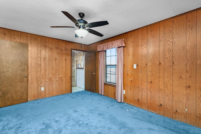 carpeted spare room featuring ceiling fan, a textured ceiling, and wooden walls