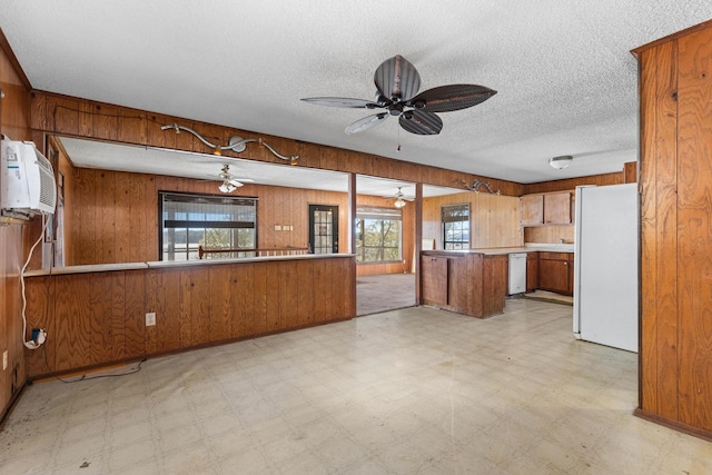 kitchen featuring kitchen peninsula, white appliances, a wealth of natural light, and wooden walls