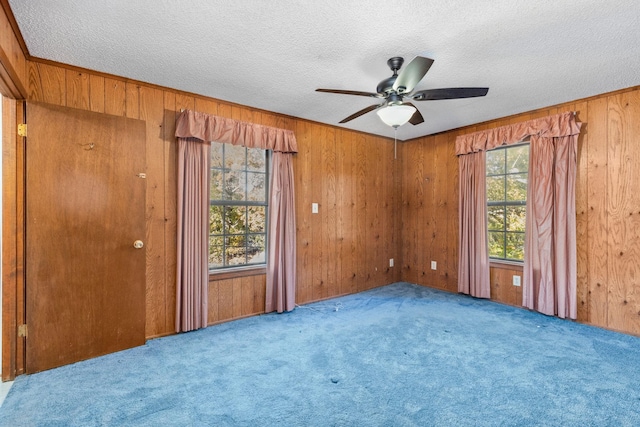 carpeted empty room with wooden walls, ceiling fan, and a textured ceiling