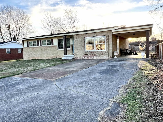 view of front of house featuring aphalt driveway, an attached carport, brick siding, and fence