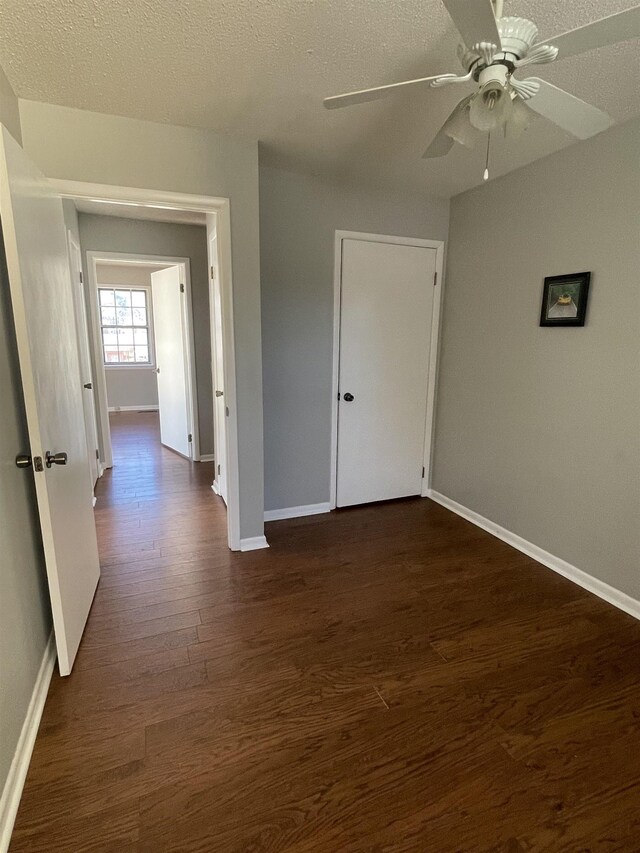 empty room with a textured ceiling, ceiling fan, and dark hardwood / wood-style flooring