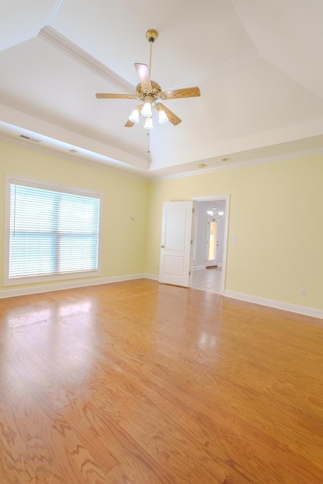 spare room with light wood-type flooring, ceiling fan with notable chandelier, a raised ceiling, and crown molding