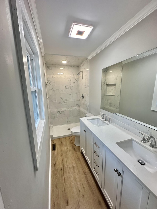 bathroom featuring vanity, hardwood / wood-style flooring, toilet, ornamental molding, and tiled shower