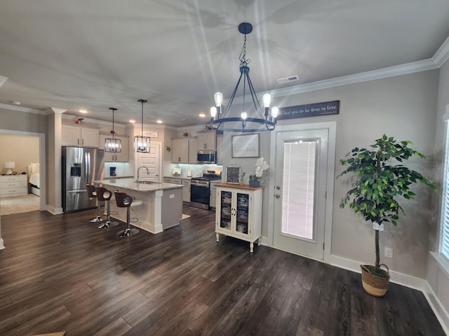 kitchen with a kitchen bar, stainless steel appliances, sink, pendant lighting, and an island with sink