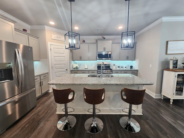 kitchen featuring a kitchen island with sink, sink, stainless steel appliances, and decorative light fixtures