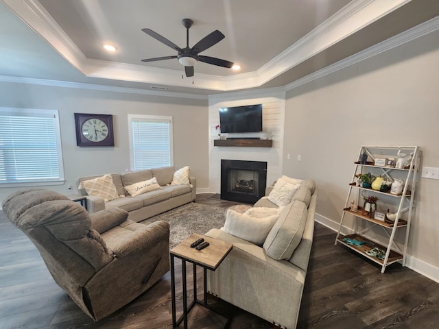 living room featuring ceiling fan, a raised ceiling, dark hardwood / wood-style flooring, a fireplace, and ornamental molding