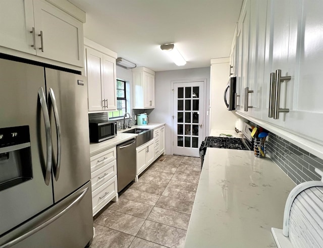 kitchen featuring appliances with stainless steel finishes, backsplash, a sink, white cabinetry, and light stone countertops