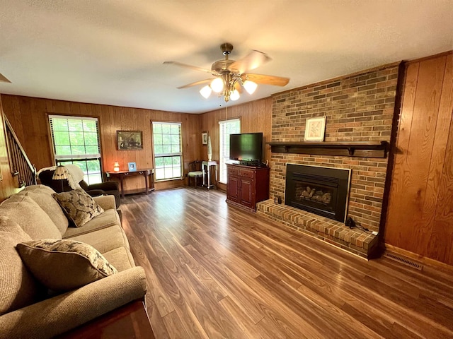 living room featuring a ceiling fan, wood finished floors, wood walls, a fireplace, and baseboards
