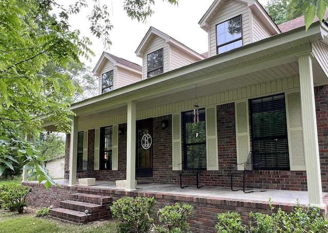 doorway to property featuring a porch and brick siding