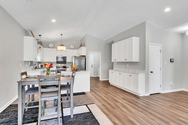 kitchen featuring lofted ceiling, light wood-style flooring, appliances with stainless steel finishes, a peninsula, and a sink