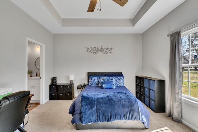 carpeted bedroom with a raised ceiling, multiple windows, baseboards, and ensuite bathroom