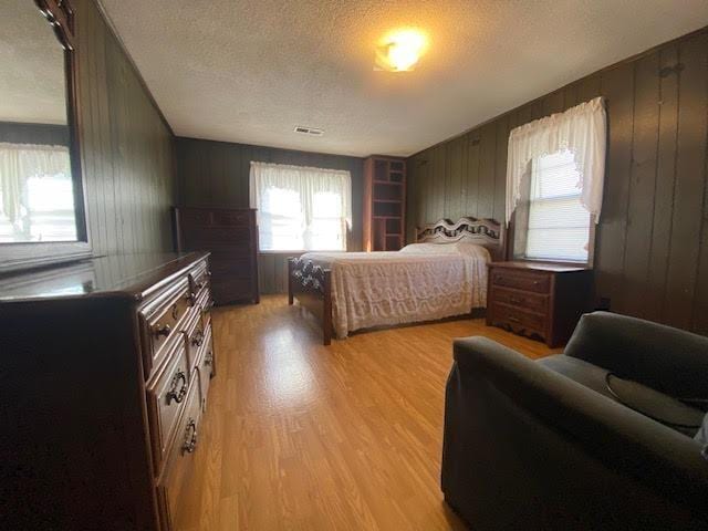 bedroom featuring wooden walls, visible vents, light wood finished floors, and a textured ceiling