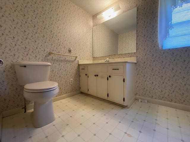 bathroom with tile patterned floors, toilet, wallpapered walls, baseboards, and vaulted ceiling