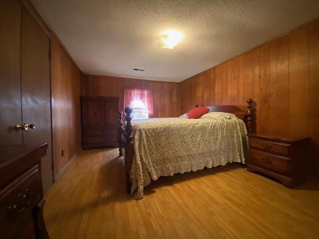 bedroom featuring light wood-style flooring, visible vents, wood walls, and a textured ceiling